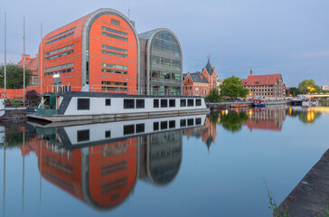 View of the Bydgoszcz waterfront featuring a modern glass building and a historic red brick...