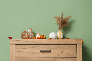 Burning candles in shape of pumpkins and autumn leaves on commode near green wall at home