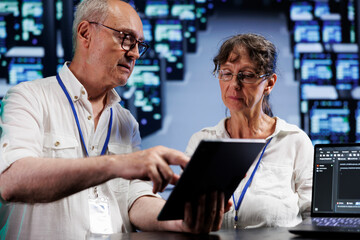 Senior trained wiremen running analysis on blade servers helping businesses manage databases, host websites and store files. Competent electricians auditing high tech data center electronics