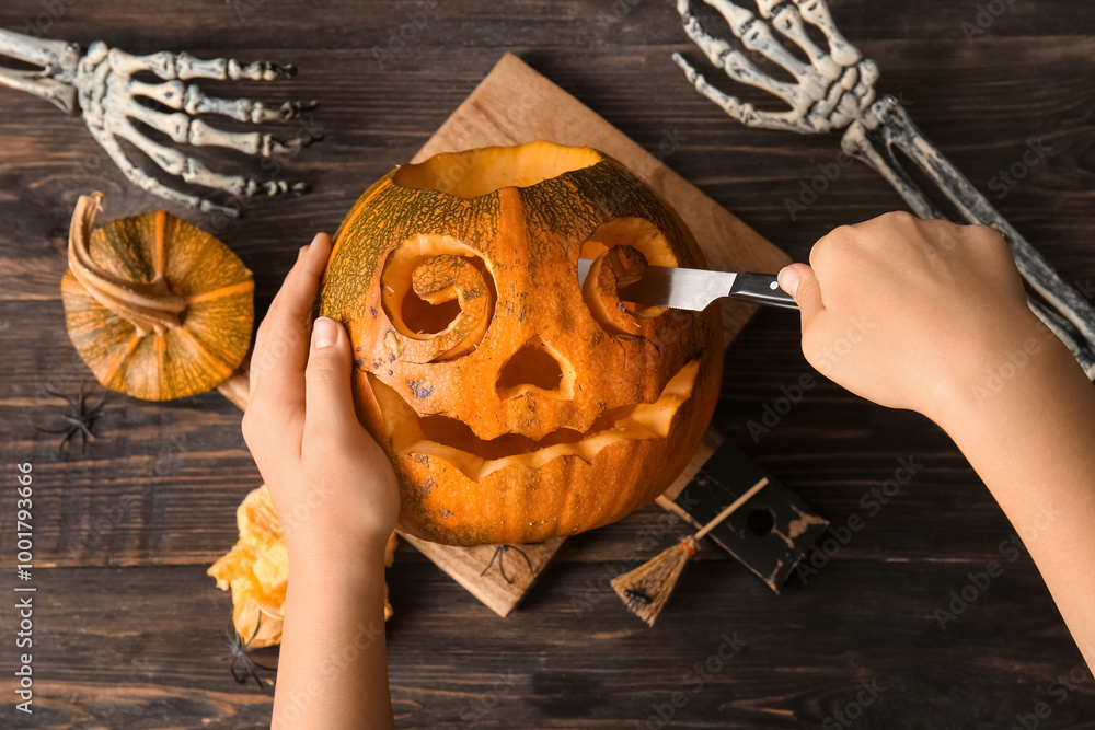 Canvas Prints Woman with skeleton hands and knife carving Jack-O-Lantern pumpkin for Halloween on brown wooden background