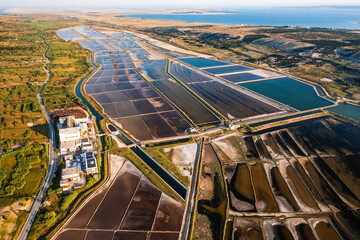 Aerial view of vibrant salt pans reflecting sunset hues near a serene coastline and lush landscape. 