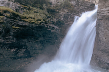 close up view of a tall waterfall in between tall rocky cliffs in summer with rushing water