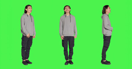 Obraz premium Cheerful male model laughing in studio, posing and being positive against full body greenscreen backdrop. Asian man smiling in studio, showing amusing funny expressions, relaxed guy.