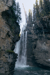 A stunning photograph capturing a majestic waterfall plunging into a pool surrounded by rocky cliffs and tall trees, evoking a sense of tranquility and natural beauty.