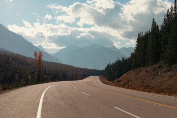 view of a road in the mountains with white and yellow lines  and clouds in the sky in fall