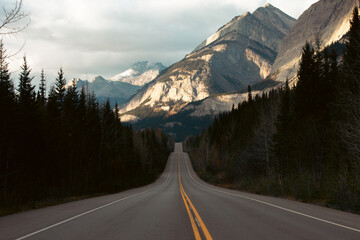 view of a road in the mountains going up and down with a tall mountain in the distance with light on it in fall
