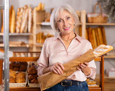 Mature female shopper with paper bag of fresh bread and baguettes in bakery