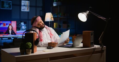 Arab worker answering phone call while remotely working from cozy home office. Teleworker talking with colleague using smartphone, discussing paperwork and tasks needing to be solved