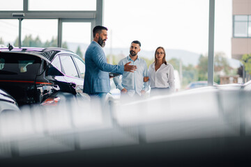 Couple and dealer discussing car options in dealership showroom.