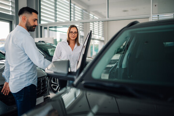 Man assisting woman in entering modern vehicle at dealership