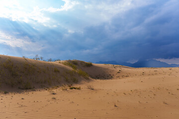 Expansive sand dunes under a dramatic cloudy sky