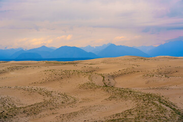Expansive desert dunes under a dramatic sky with distant mountains