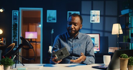 BIPOC content creator filming technology review of newly launched V mount battery, unpacking it and presenting specifications to audience. Internet star showing charging device to viewership