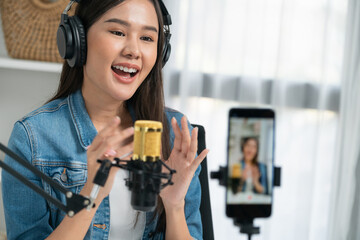 Host channel Asian influencer talking in broadcast wearing headsets on social media live on smartphone recording online, greeting listeners with coaching life or business at modern studio. Stratagem.