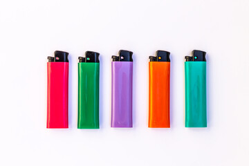 Five lighters of different colors, pink, green, purple, orange and blue lie on a white background