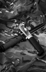 Naklejka premium Two fixed stainless steel knives crossed with each other, a tourist one with a black handle and a military one with a green handle, on a pixelated background. Black and white vertical photo, top down.