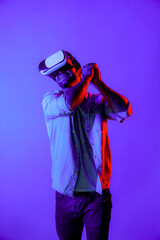 Caucasian man with VR glasses equipment moving in golf playing gesture while standing at neon...