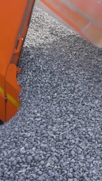 A dump truck is dumping gravel at the excavation site. Stock footage. Close up of unloading process of a construction truck full of small stones.