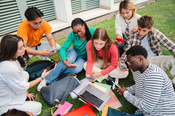 Diverse group of students sitting on the university campus lawn, using cellphones and reviewing notes together for a collaborative study session in an outdoor, relaxed setting. Highschool classmates