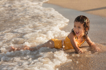Little toddler girl with happy smile enjoying water at sandy beach, childhood memories and summer vacation concept
