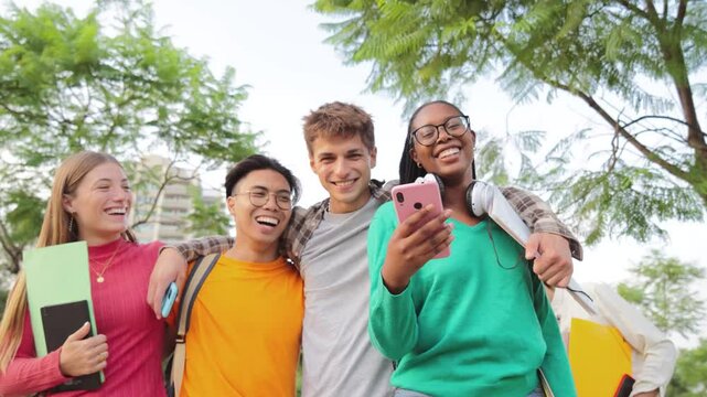 Group of multiracial students walking together at university campus and watching the social media on a smartphone. Happy internacional teenage classmates laughing while going to class. Slow motion