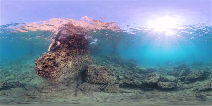 Panorama spherical VR. Two divers explore an underwater reef, one sitting on a rock and the other diving into the water. The scene is captured in 360 view, emphasizing the vibrant underwater environme