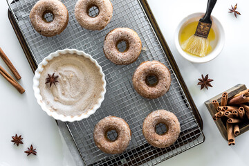 Homemade doughnuts on a cooling rack with cinnamon sugar and melted butter.