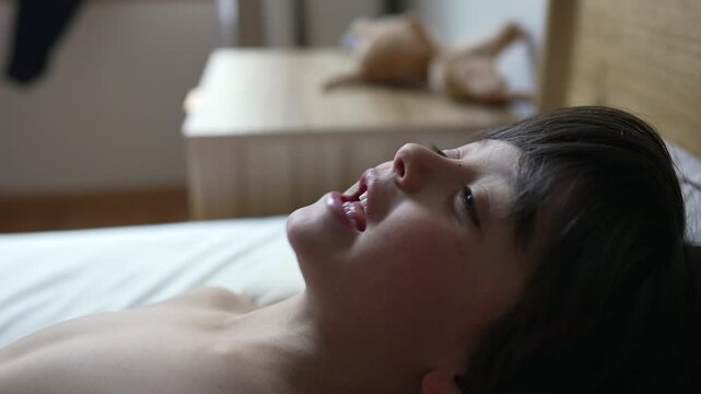 young boy smiling in bed during early morning carefree and joyful moments in a cozy home warm light illuminating his happy face childhood innocence and comfort in familiar surroundings