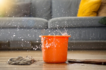 Water dripping from ceiling into plastic bucket on floor in living room. Leaking roof concept.  © Queenmoonlite Studio