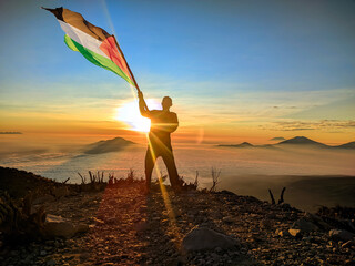 man raising the flag of palestine on the top of the mountain. background of mountains at sunset or sunrise. palestine flag for Independence Day.
