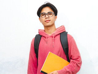 Portrait of a smiling confident Asian male college student wearing a pink hoodie and carrying a...