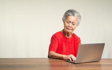 Elderly woman in a red shirt using a laptop on a wooden table.