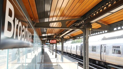 Obraz premium New York subway station Broadway text sign. Metropolitan train on platform, United States public metro transportation. Elevated outdoor railway line, Astoria, Queens. NYC passenger railroad traffic.