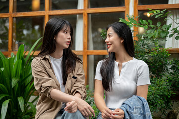 Two young Asian female friends are engaged in conversation in a beautiful garden.