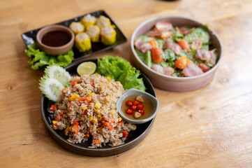 A wooden dining table featuring a plate of fried rice, a salad bowl, and a plate of steamed dumpling
