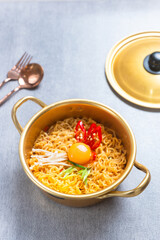 Ramyeon or Ramyun with spicy flavour topped with egg yolk, chilli, vegetables in a traditional Korean noodle pot. Serving a Korean style instant noodle. Perfect for recipe, article, catalogue.