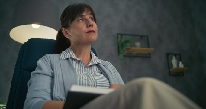 Close up of professional therapist sitting in chair, listening attentively to patient, taking notes in notebook. Female psychologist conducts counseling or therapy session. Psychological assistance.