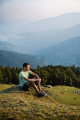 This Handsome male hiker smiling while seated on a mountain top in himachal pradesh india.
