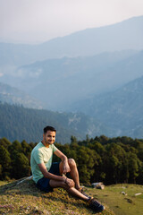 This Handsome male hiker smiling while seated on a mountain top in himachal pradesh india.

