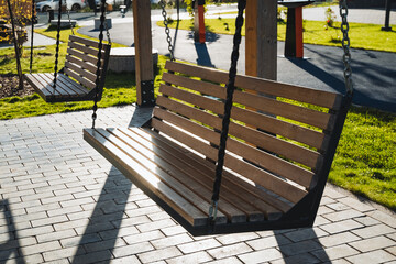 In a serene park, a rustic wooden swing hangs from sturdy chains, inviting visitors to relax and enjoy a delightful moment in natures refreshing air and stunning beauty