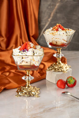 Glass ice-cream bowls with strawberries and cream on colorful background