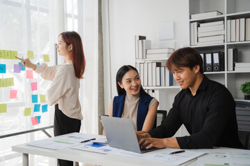 Creative Collaboration: A team of Asian business professionals brainstorm innovative ideas, using sticky notes and a laptop in a modern office setting. This image embodies the spirit of teamwork.