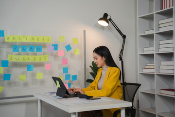 Focused on Success: A young businesswoman in a yellow blazer, engrossed in her work on a laptop,...