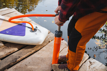 A person is actively pumping air into a paddle board while it is resting on a dock, preparing for an exciting adventure on the water later. This is part of their outdoor recreation plans