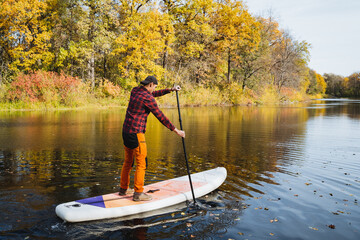 A man is enjoying the experience of riding a paddle board on a serene lake surrounded by nature and...