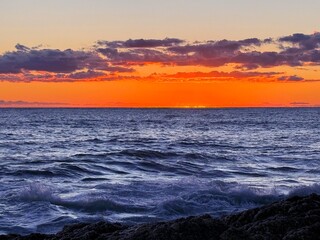 Naklejka premium Sunset clouds over sea waves and rocky coast. 