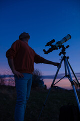 Amateur astronomer looking at the evening skies, observing planets, stars, Moon and other celestial objects with a telescope.