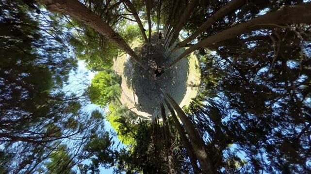 Tiny Planet effect in a forest, with a person at the center, surrounded by tall trees creating a circular world-like illusion, offering a surreal view of the natural environment.