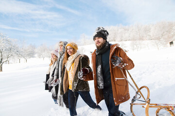 Group of friends pulling sleds behind them, going to sleddingin in snowy nature. First snowfall of the season.