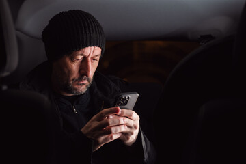 Adult caucasian male reading text message on cellular phone while sitting at the back seat of the car at night